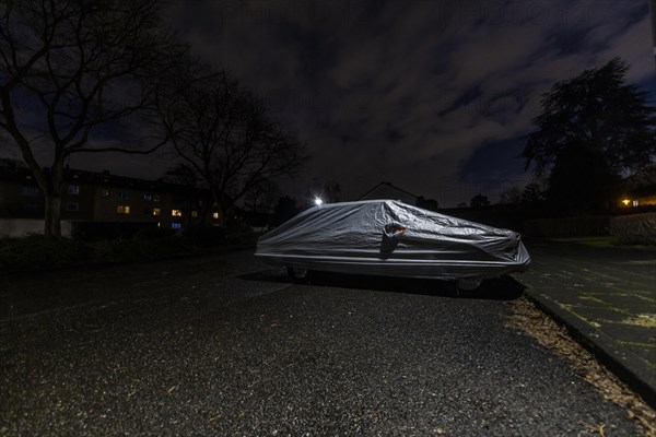 Covered car parked on the street under a lamppost at night