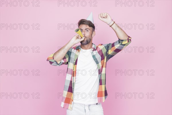 Man raising his arms while blowing party horn pink background