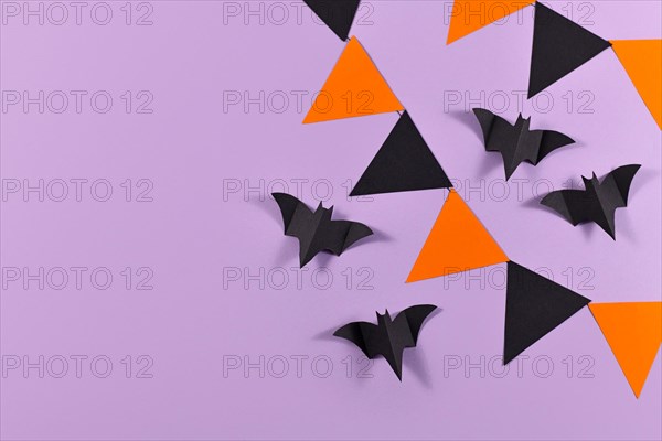 Halloween background with garlands and paper bats in traditional colors orange and black on violet background with copy space