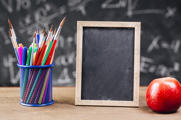 Pen stand blank chalkboard with apple placed desk