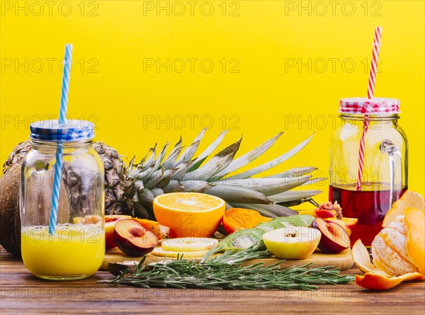 Fruits rosemary juice mason jar chopping board against yellow backdrop