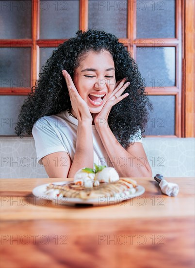 Happy girl looking at a plate of chocolate crepe and ice cream on table. Excited woman looking at a chocolate crepe and ice cream on the table