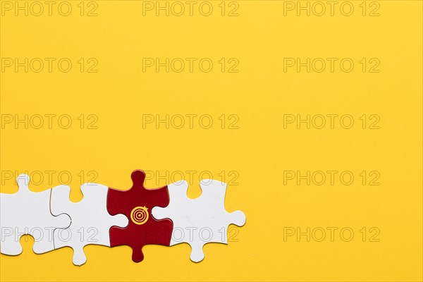 Red jigsaw puzzle piece with dartboard symbol arranged with white piece yellow background