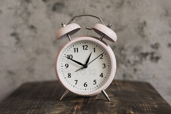 Pink alarm clock wooden desk against weathered wall