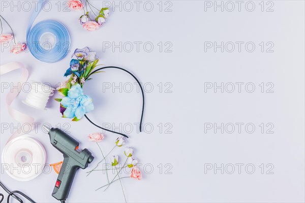 Overhead view blue white ribbon artificial flower glue gun making hairband white backdrop