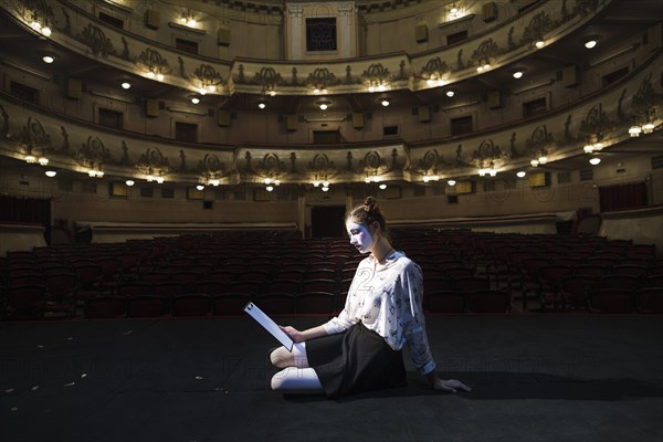 Side view female mime sitting stage reading manuscript