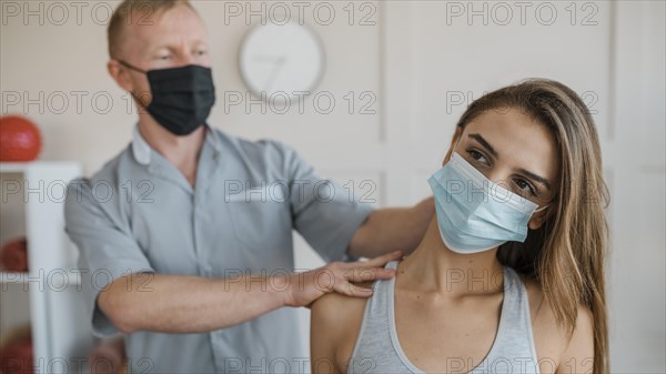 Male physiotherapist wearing medical mask during therapy session female patient