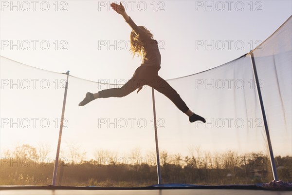 Active little girl jumping trampoline against sky