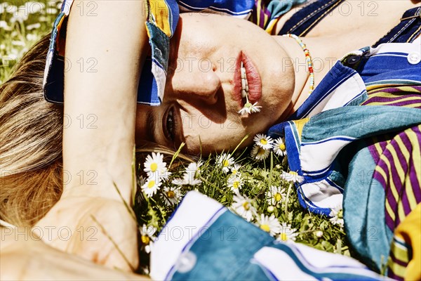 Pretty young woman lying in the grass between daisies with a daisy in her mouth