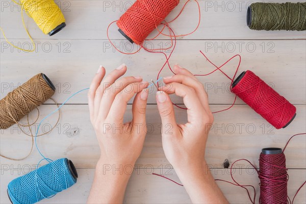 Woman s hand inserting blue yarn needle wooden table