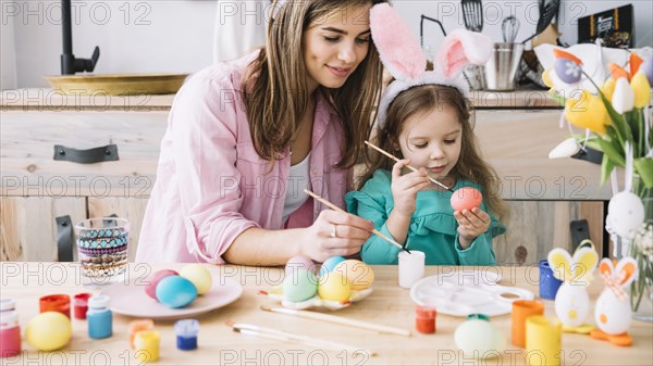 Little girl mother painting eggs easter