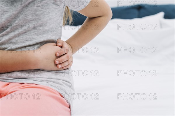 Mid section girl touching her wrist with hands sitting bed