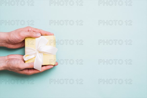 Person s hand holding small gift box against blue background