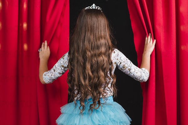 Rear view girl long brunette wavy hair looking from red curtain