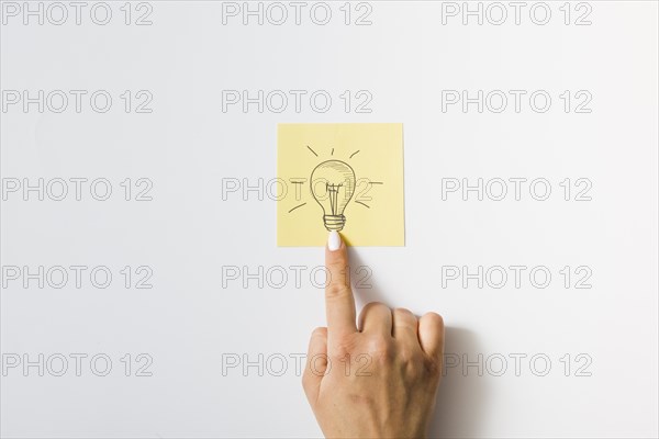 Close up person touching finger drawn light bulb sticky note