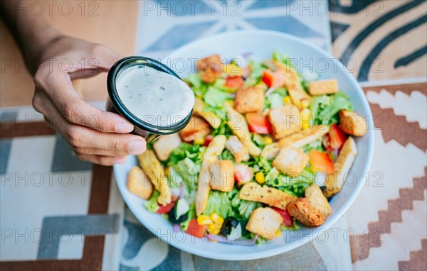 Concept of healthy food and lifestyle. Hand putting dressing on a caesar salad