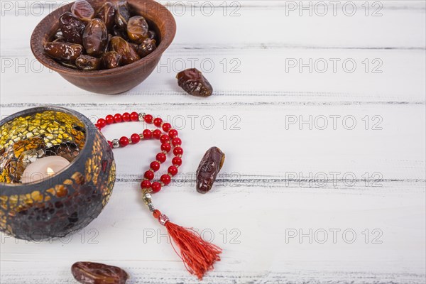 Lighted candle with bowl juicy dates red prayer beads white wooden background