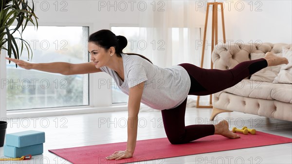 Side view pregnant woman doing yoga home