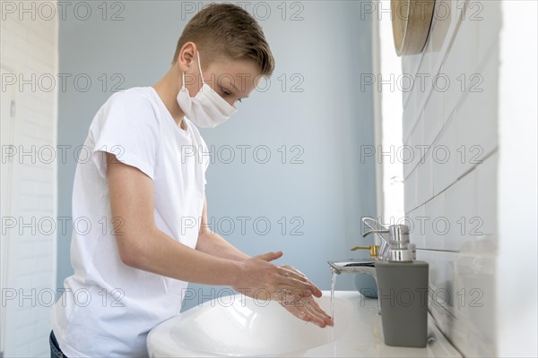 Boy wearing medical mask washing his hands side view