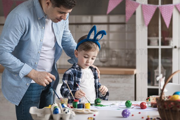 Father teaching little boy how paint eggs easter