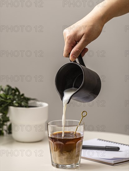 Person pouring cream coffee glass