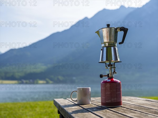 Espresso pot on a gas cooker next to a cup standing on a wooden table at the lake