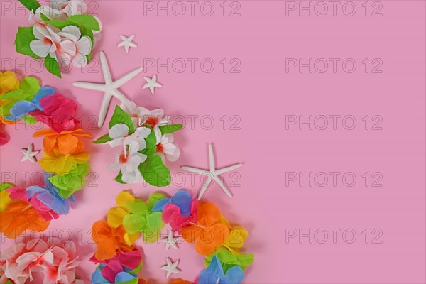Bright flower lei necklaces on side of pink background with copy space