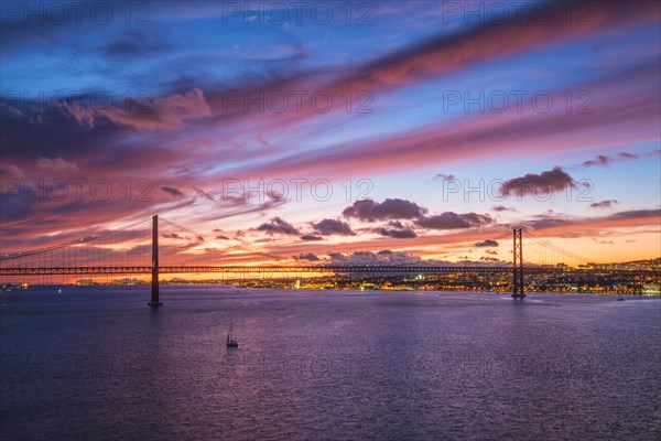 View of 25 de Abril Bridge famous tourist landmark of Lisbon connecting Lisboa and Almada on Setubal Peninsula over Tagus river in the evening twilight with boats. Lisbon