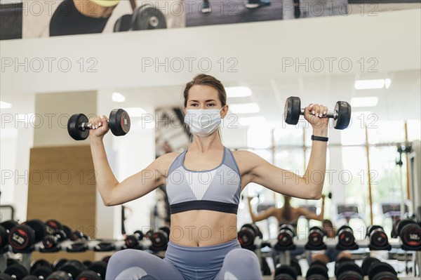 Woman with medical mask exercising gym during pandemic