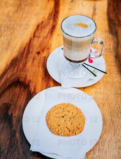 Close up of cookie and cappuccino on wooden table. Top view glass of hot cappuccino with cookie on wooden background
