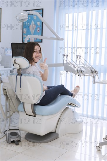 Smiling female patient sitting chair showing thumb up dental clinic
