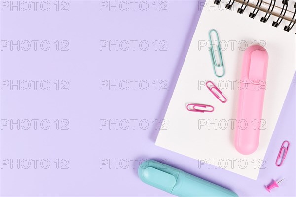 Clipboard with pink and blue text markers and paper clips on purple background with empty copy space