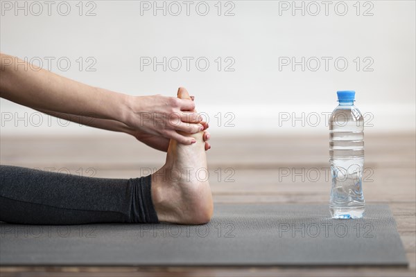 Side view woman stretching yoga mat with water bottle