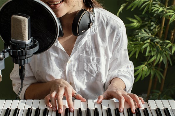 Smiley female musician playing piano keyboard indoors singing into microphone