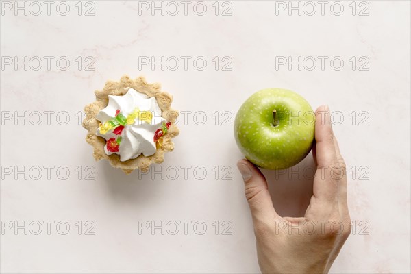 Human hand holding green apple near tart cake backdrop