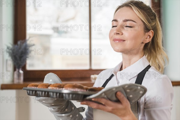 Close up smiling young woman smelling fresh baked muffins