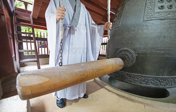 Korean monk strikes the bell with a wooden trunk