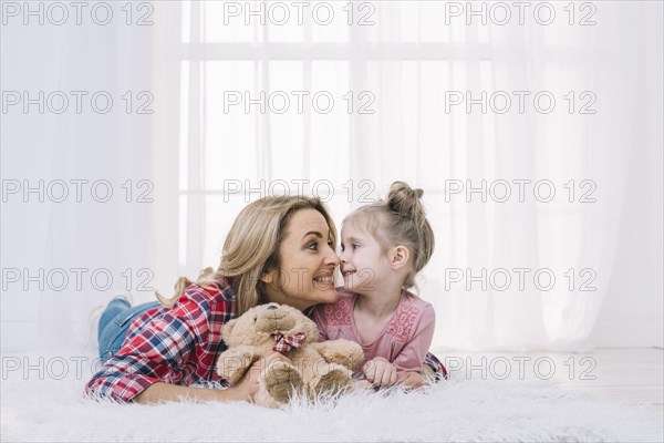 Beautiful mother daughter lying fur making funny face with teddy bear