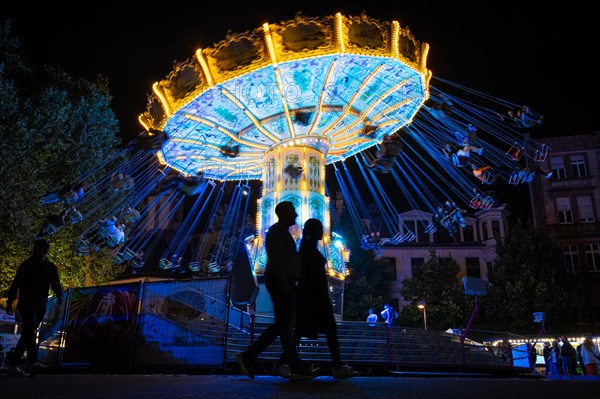 The colourful lights of the carousel at the Mainfest glow in the evening. The Mainfest on the Mainkai