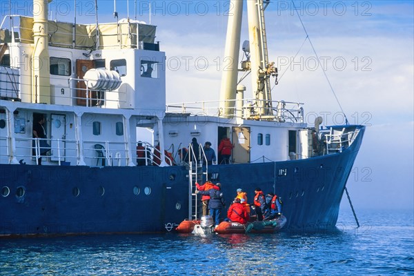 People climbing aboard a ship from an inflatable boat