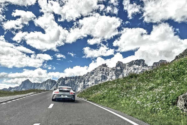 Photo with reduced dynamic range saturation HDR of view of Porsche 911 GT3 driving on mountain road above tree line pass road alpine pass mountain pass in high alps