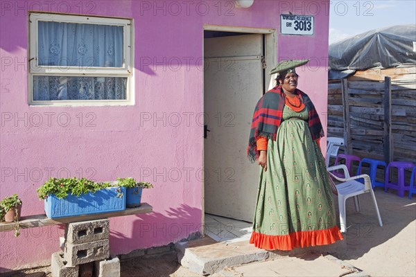 Herero woman in traditional colourful dress in front of her house in township near Swakopmund