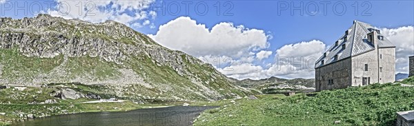 Photo with reduced dynamics saturation HDR of view on left mountain lake right historical hotel accommodation Ospizio San Gottardo Sankt Gotthard Hospice with historical building fabric from year 1237 13th century on 2091 metres high Gotthard Pass