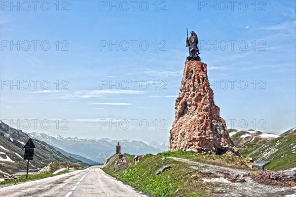 Photo with reduced dynamic saturation HDR of mountain pass alpine mountain road alpine road pass road pass above tree line with right monument with statue of Saint Bernard of Menthon on top of Little Saint Bernard Pass
