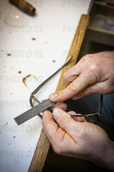 An optician files the frame of a pair of glasses with a file