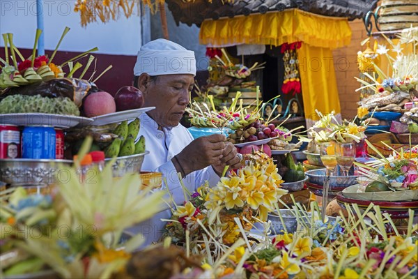 Balinese man preparing food offerings for traditional Hindu ceremony in village Padang Bai