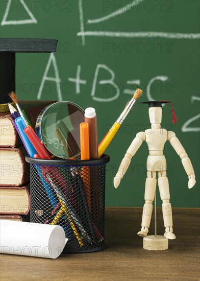 Front view wooden figurine with academic cap books