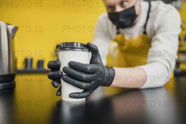 Barista with medical mask gloves holding coffee cup