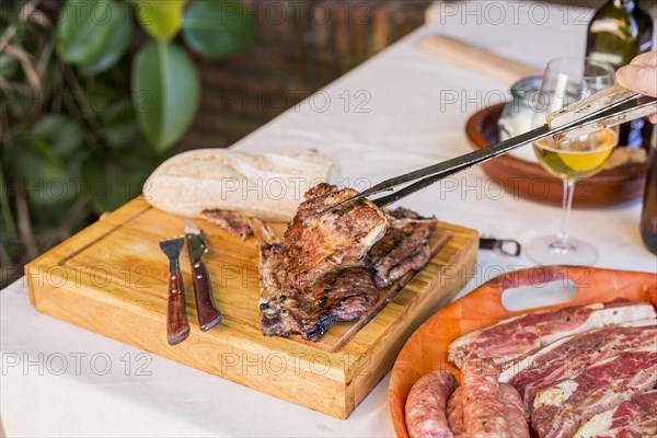 Person holding fresh grilled beef steak with tong wooden board