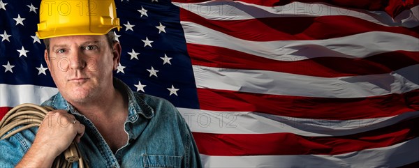 Male contractor wearing blank yellow hardhat over waving american flag background banner